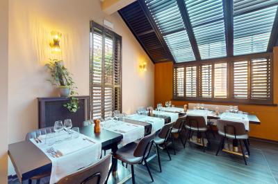 Salle de restaurant avec tables dressées, banquettes en bois, bar en bois et étagères garnies de verres et bouteilles.