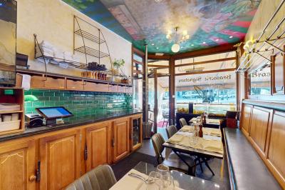 Salle de restaurant avec tables dressées, banquettes en bois, bar en bois et étagères garnies de verres et bouteilles.