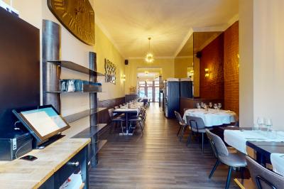 Salle de restaurant avec tables dressées, banquettes en bois, bar en bois et étagères garnies de verres et bouteilles.