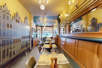 Salle de restaurant avec tables dressées, banquettes en bois, bar en bois et étagères garnies de verres et bouteilles.