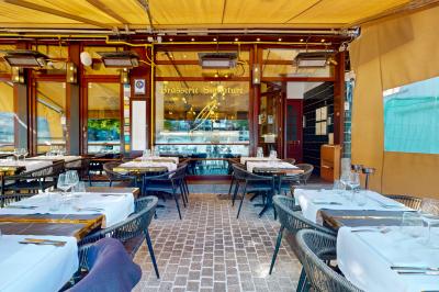 Salle de restaurant avec tables dressées, banquettes en bois, bar en bois et étagères garnies de verres et bouteilles.