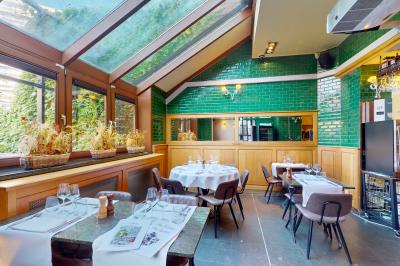Salle de restaurant avec tables dressées, banquettes en bois, bar en bois et étagères garnies de verres et bouteilles.