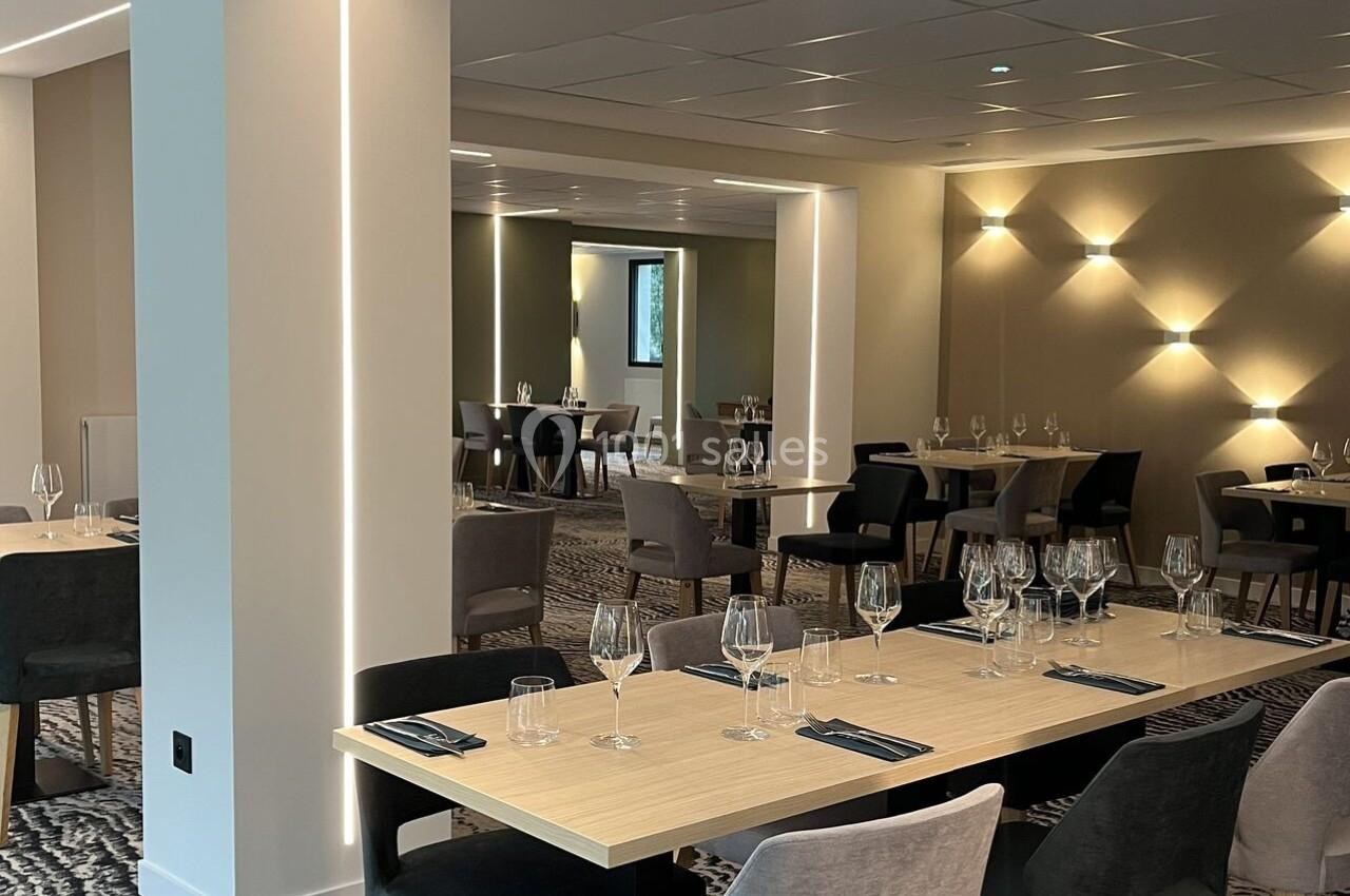 Salle de restaurant moderne avec tables en bois clair, chaises rembourrées et éclairage tamisé.