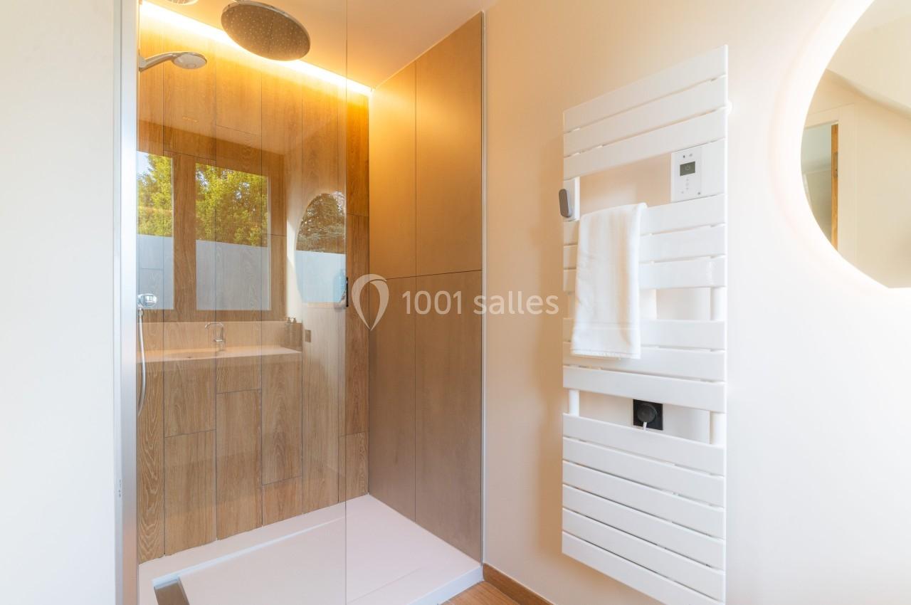 Douche moderne avec paroi vitrée, sèche-serviettes blanc et meuble en bois dans une salle de bain lumineuse.
