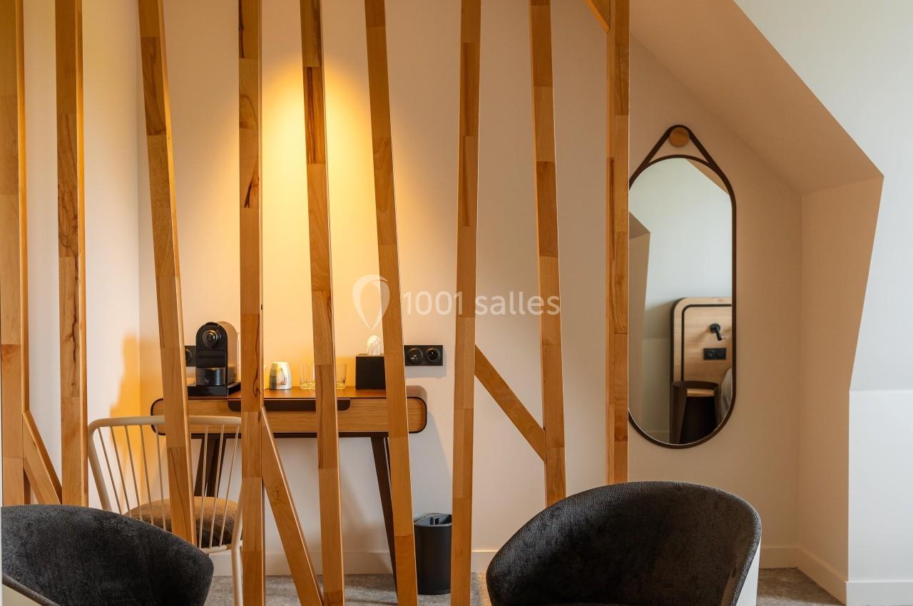 Deux fauteuils entourent une petite table devant une cloison en bois, avec un bureau et un miroir en arrière-plan.