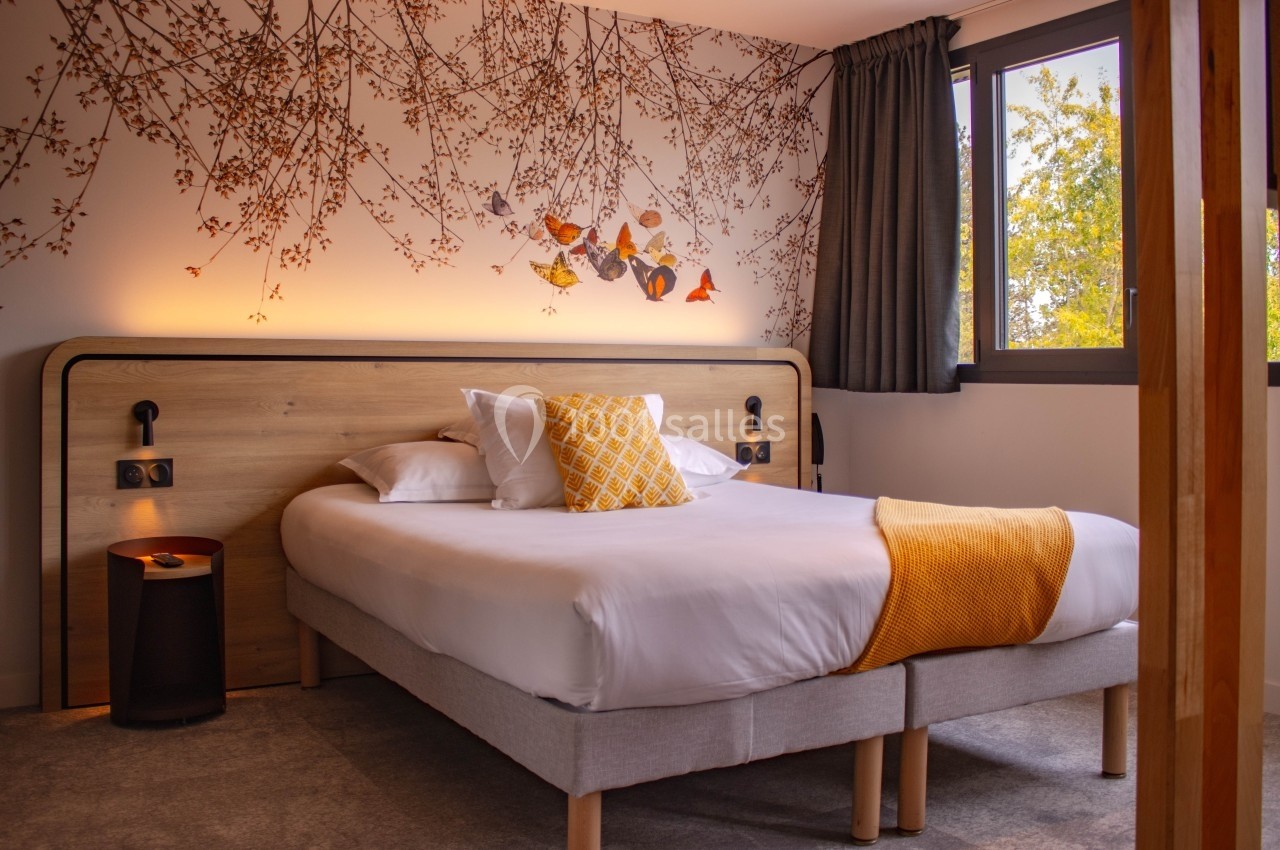 Chambre lumineuse avec un lit double, décorée de motifs végétaux sur le mur et des touches de jaune.