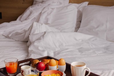 Lit avec des draps blancs, serviettes pliées au premier plan et mur décoré de branches et papillons colorés.
