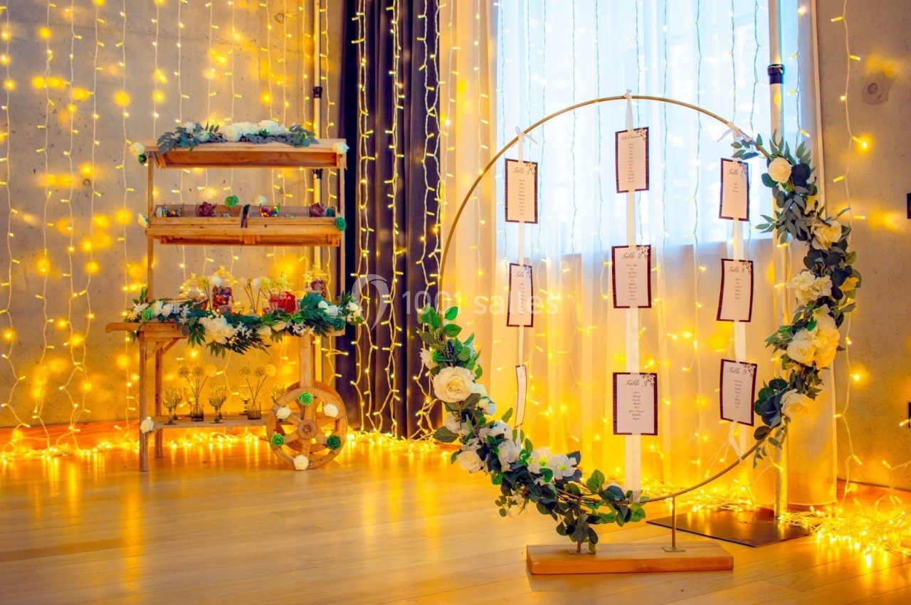 Décoration lumineuse avec un cercle fleuri portant des cartes et des étagères ornées de fleurs et guirlandes.