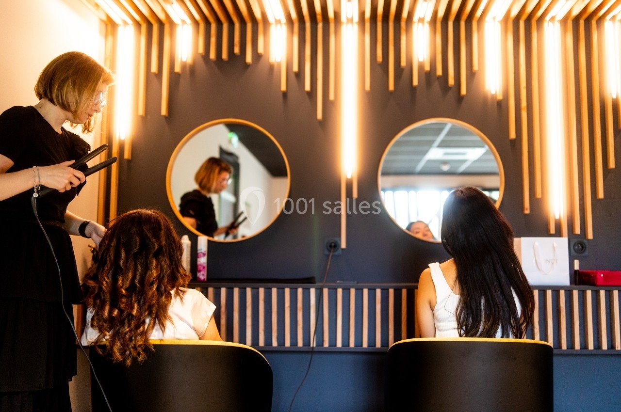 Une coiffeuse utilise un lisseur sur les cheveux d'une cliente, devant un miroir dans un salon moderne.