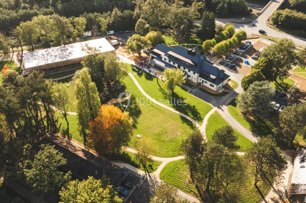 Vue aérienne d'un complexe entouré de verdure avec des bâtiments, des chemins et un parking adjacent.