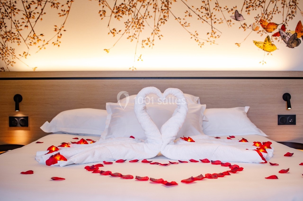 Lit décoré avec des serviettes en forme de cœur et des pétales de rose rouges, dans une ambiance romantique.