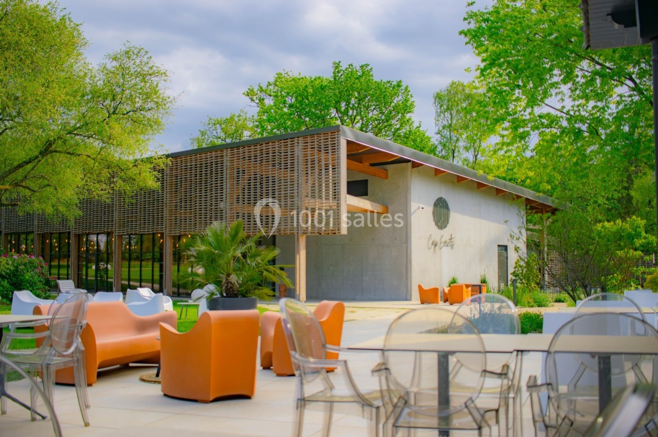 Terrasse avec mobilier coloré devant un bâtiment moderne entouré de verdure sous un ciel partiellement nuageux.