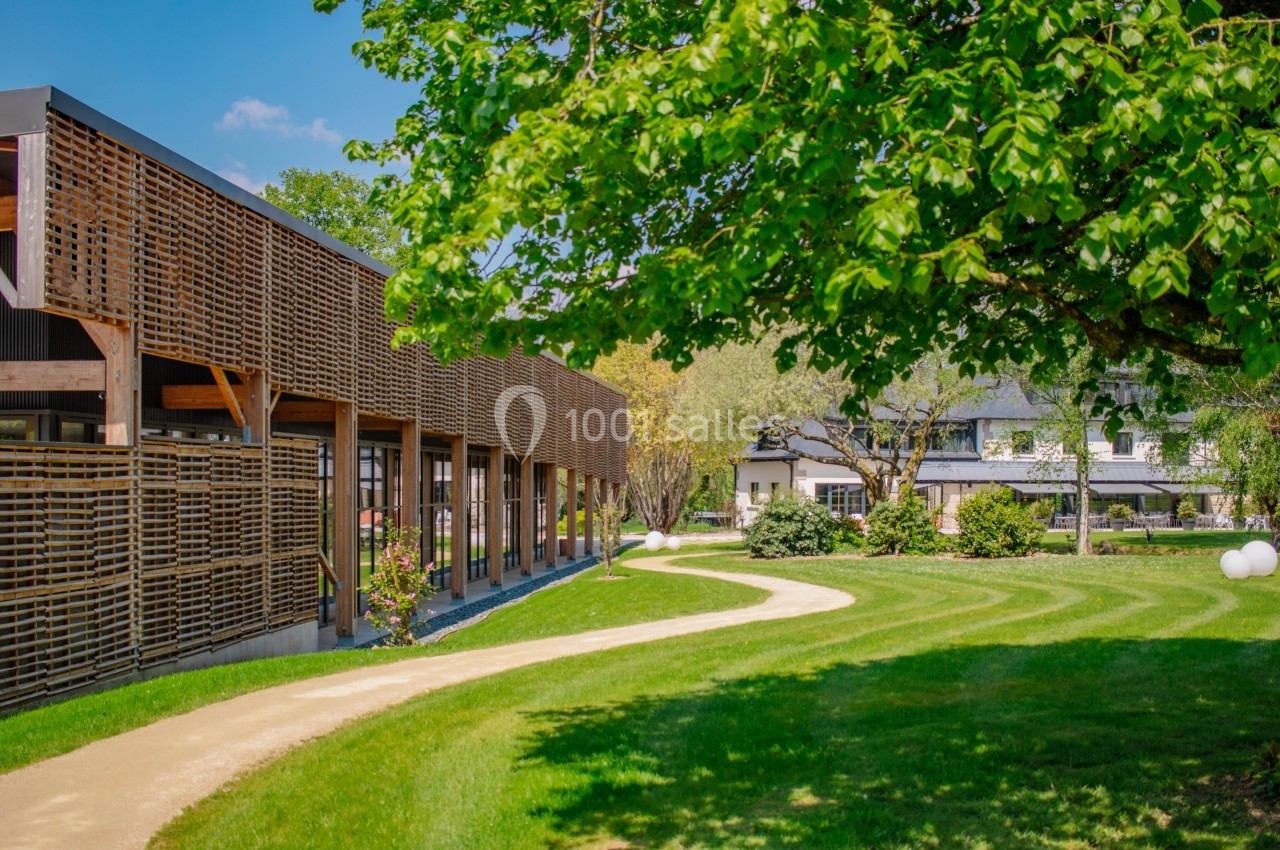 Bâtiment moderne en bois longeant un chemin sinueux dans un jardin verdoyant sous un arbre feuillu.