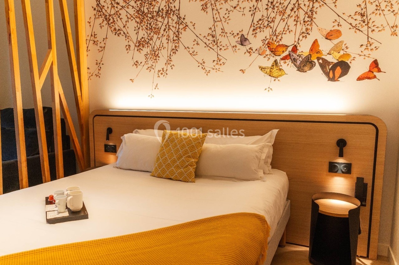 Lit double avec couverture jaune, coussin décoratif, plateau avec tasses et mur orné de motifs floraux et oiseaux.