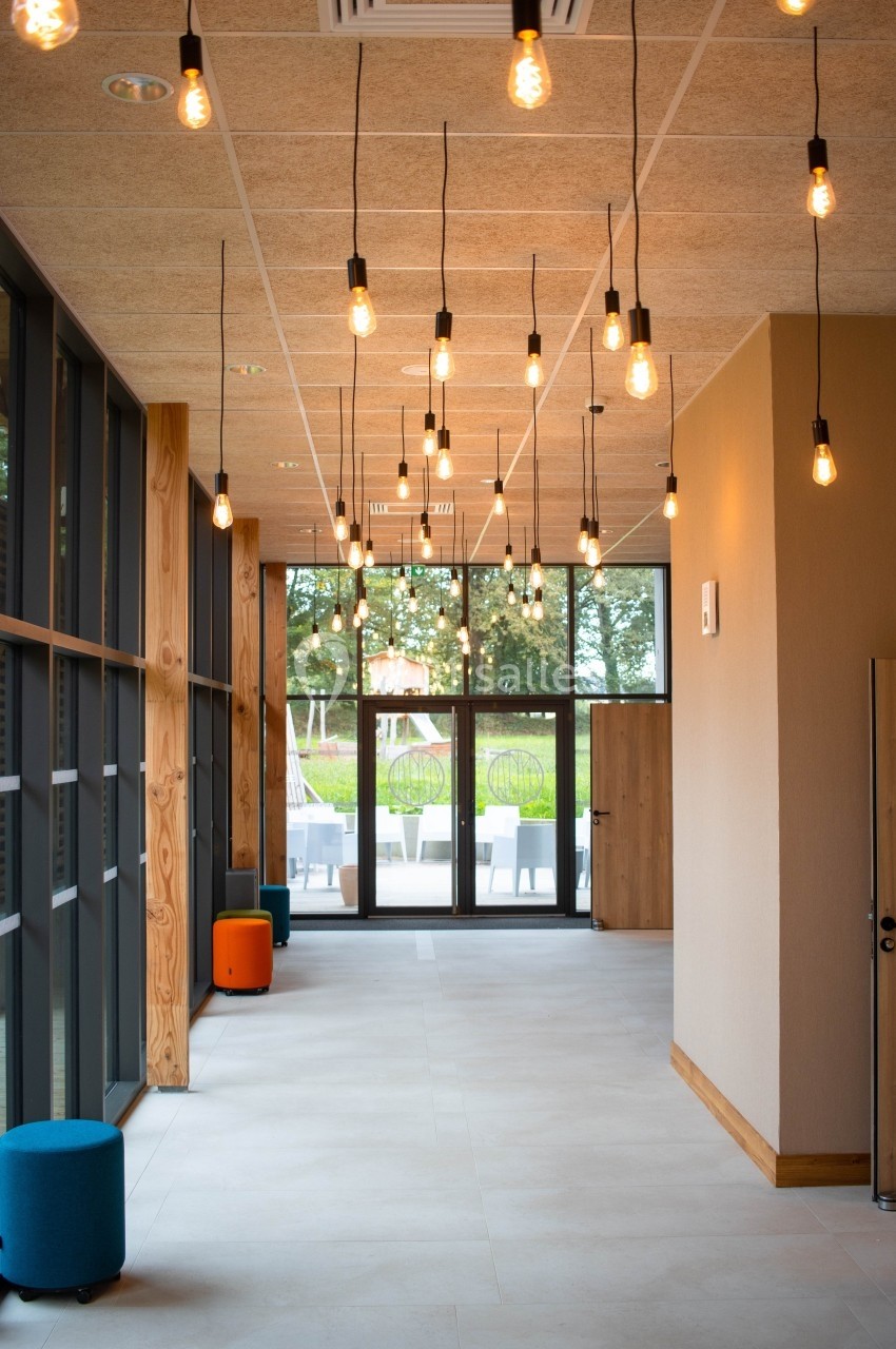 Suspension de multiples ampoules au plafond d'un couloir lumineux avec vue sur un espace extérieur verdoyant.