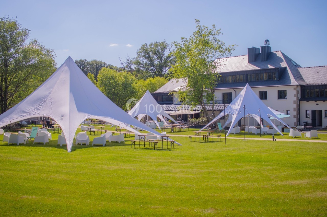 Tentes blanches modernes installées sur une pelouse verte devant un bâtiment avec terrasse, par une journée ensoleillée.
