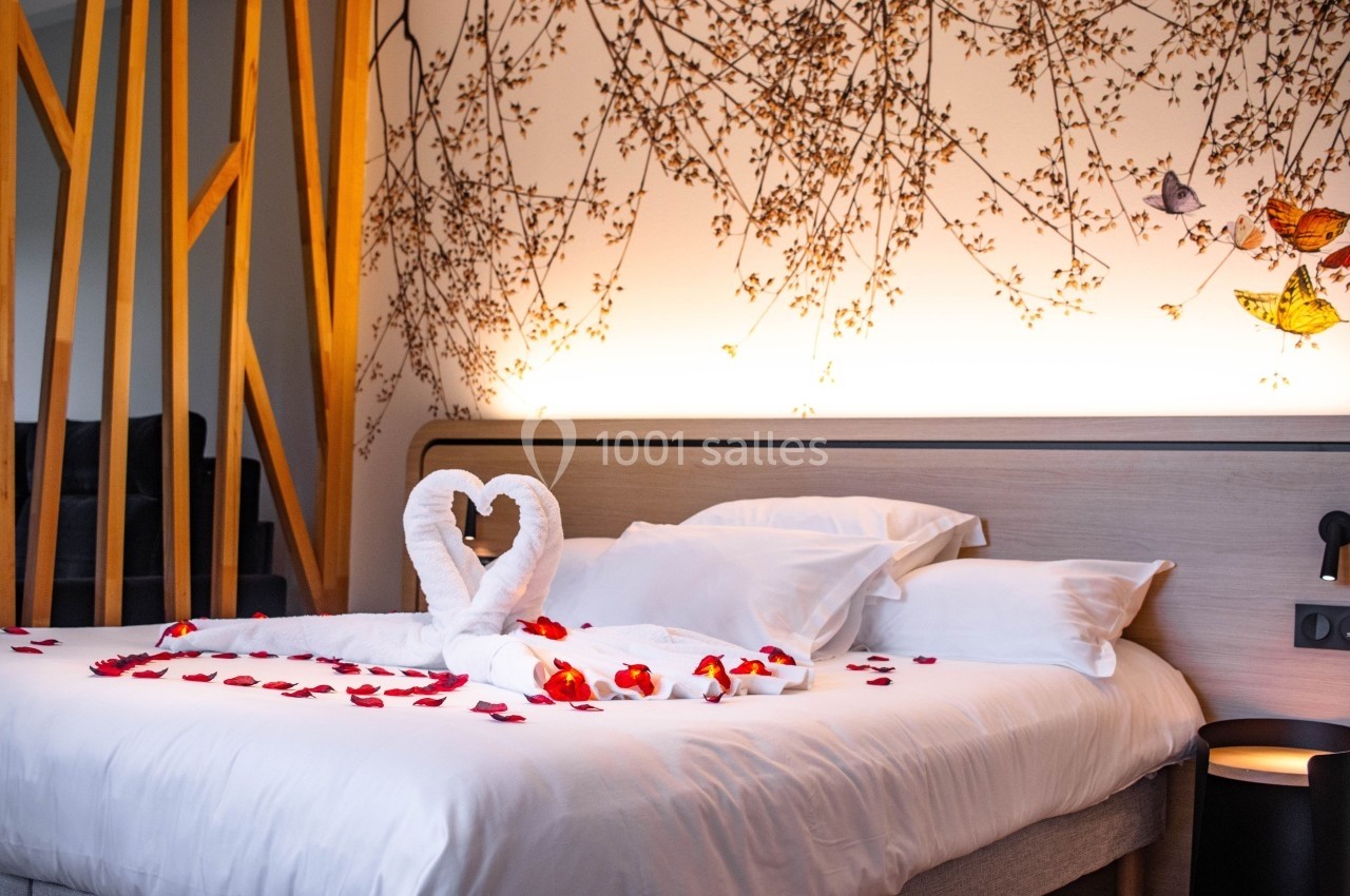 Lit décoré avec des pétales de rose, des serviettes pliées en forme de cœur et un éclairage chaleureux en arrière-plan.