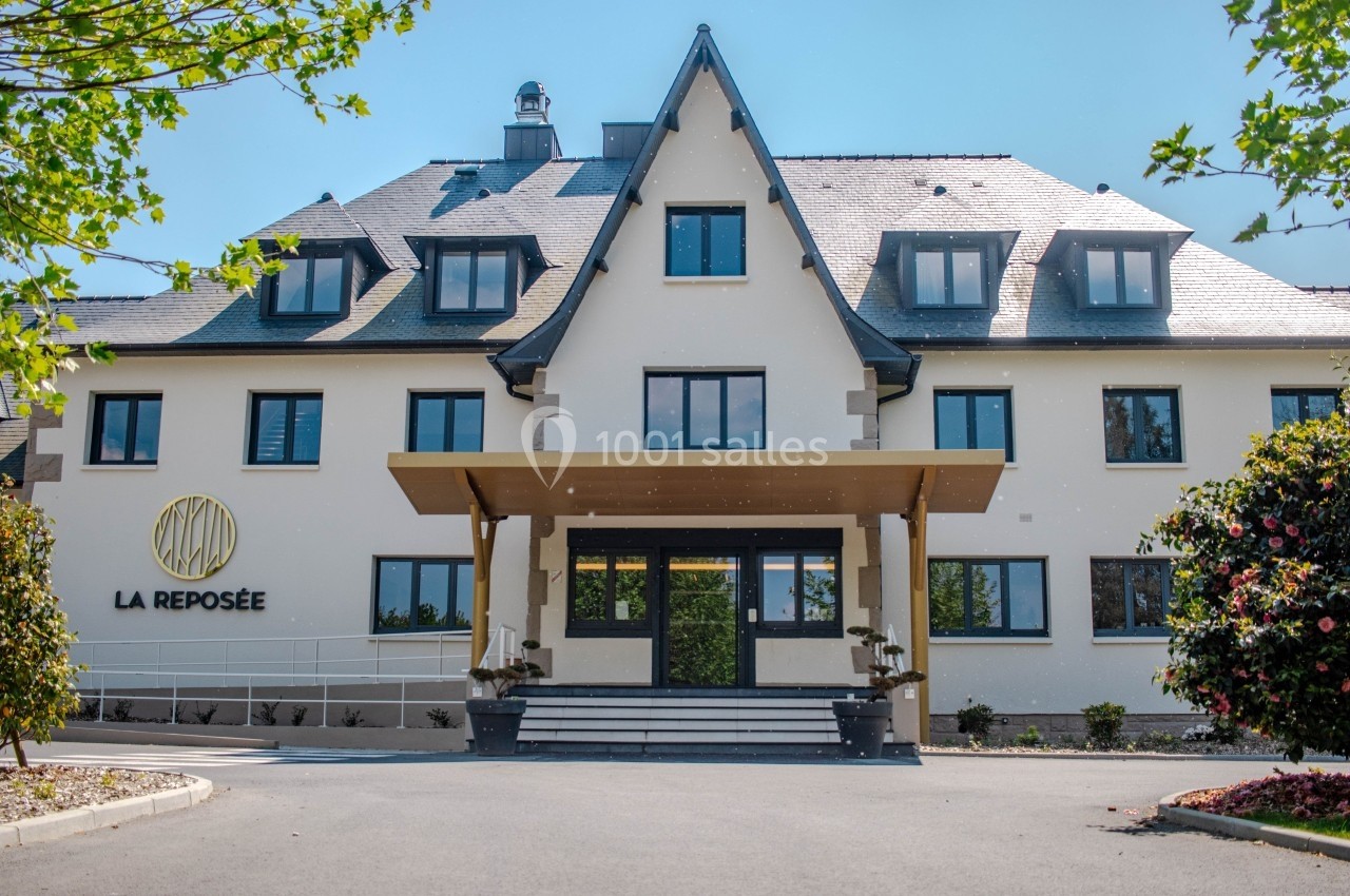 Façade d'un bâtiment moderne avec toit en ardoise, entrée principale couverte et végétation environnante.