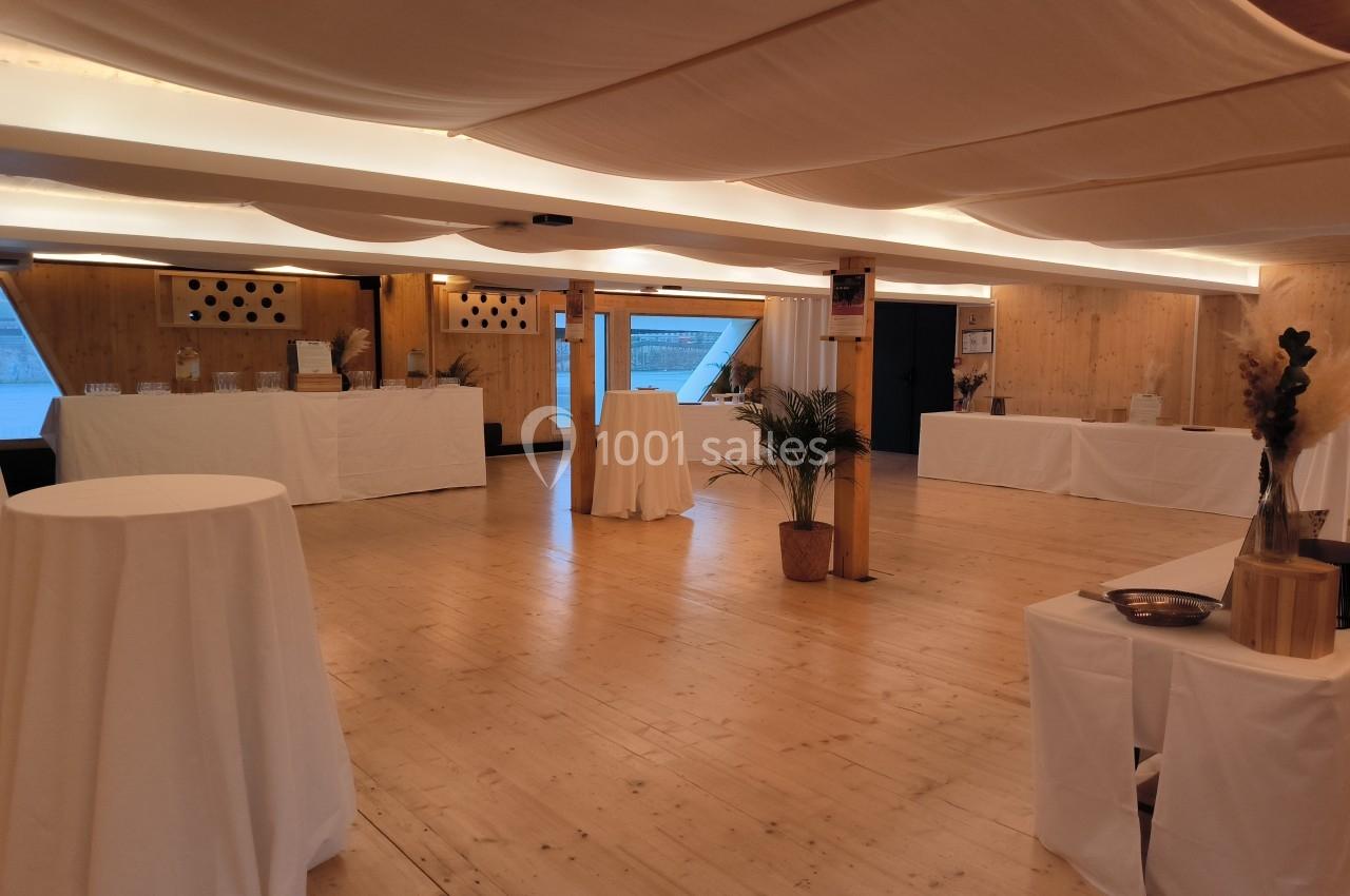 Salle lumineuse avec parquet en bois, tables hautes drapées de blanc et décorations minimalistes.