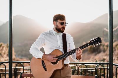 Un homme joue de la guitare acoustique en extérieur, entouré de verdure et de décorations florales.