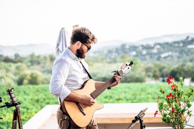 Un homme joue de la guitare acoustique en extérieur, entouré de verdure et de décorations florales.