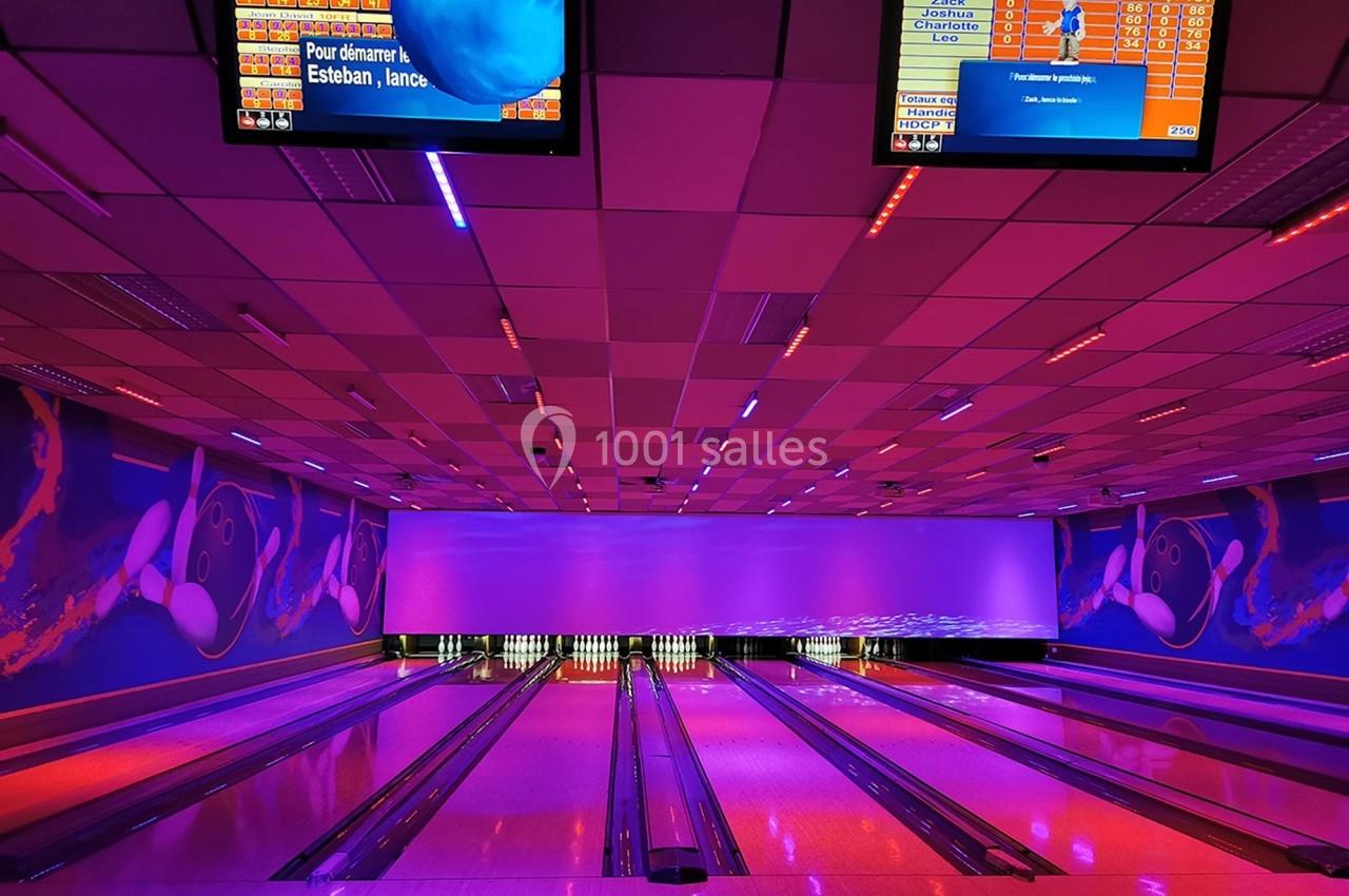 Pistes de bowling éclairées par des lumières colorées, avec écrans d'affichage des scores suspendus au plafond.