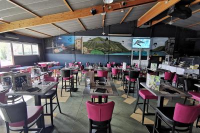 Salle de réception avec une longue table dressée, des chaises rouges et noires, et une fresque murale représentant un…