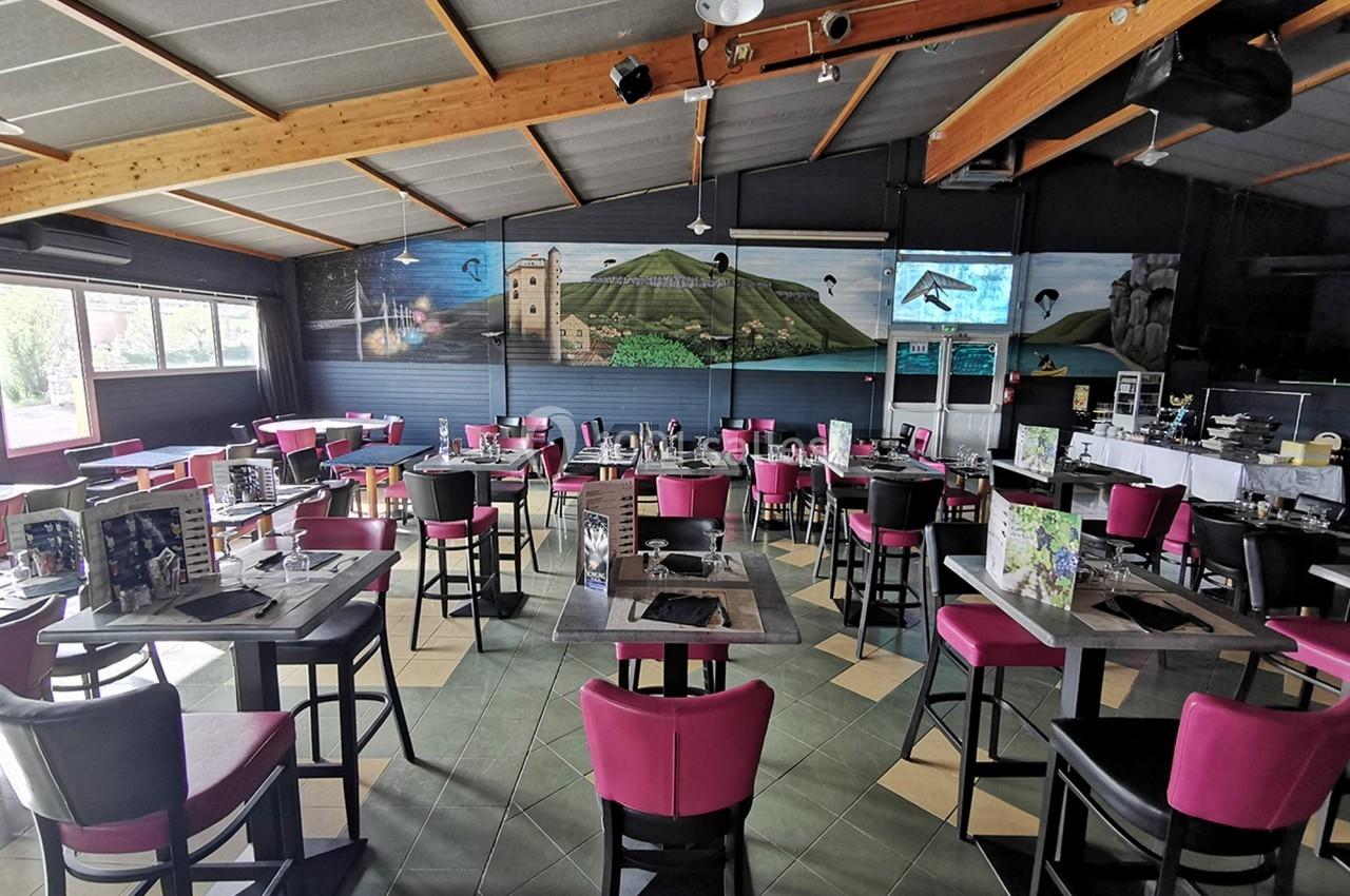 Salle de restaurant lumineuse avec tables et chaises roses, décor mural représentant un paysage rural.