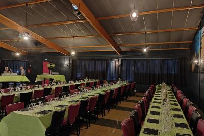 Salle de réception avec une longue table dressée, des chaises rouges et noires, et une fresque murale représentant un…