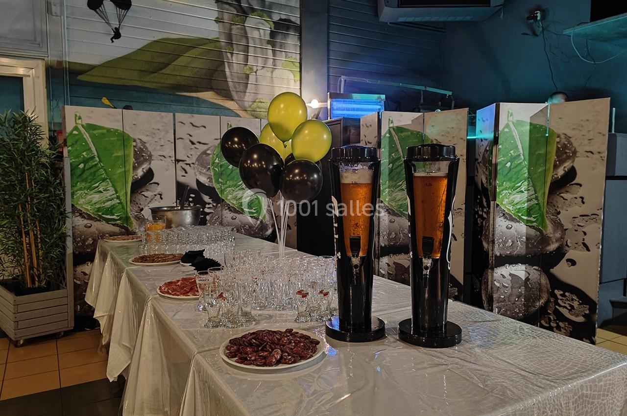 Buffet avec nappes blanches, verres, assiettes de charcuterie et deux distributeurs de boissons dans une salle décorée.