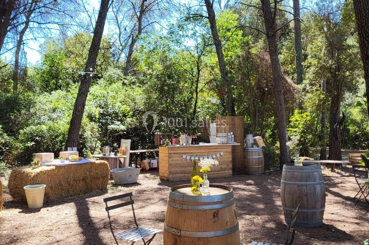 Espace extérieur boisé aménagé avec des tonneaux, des chaises et un bar en bois pour une réception en plein air.