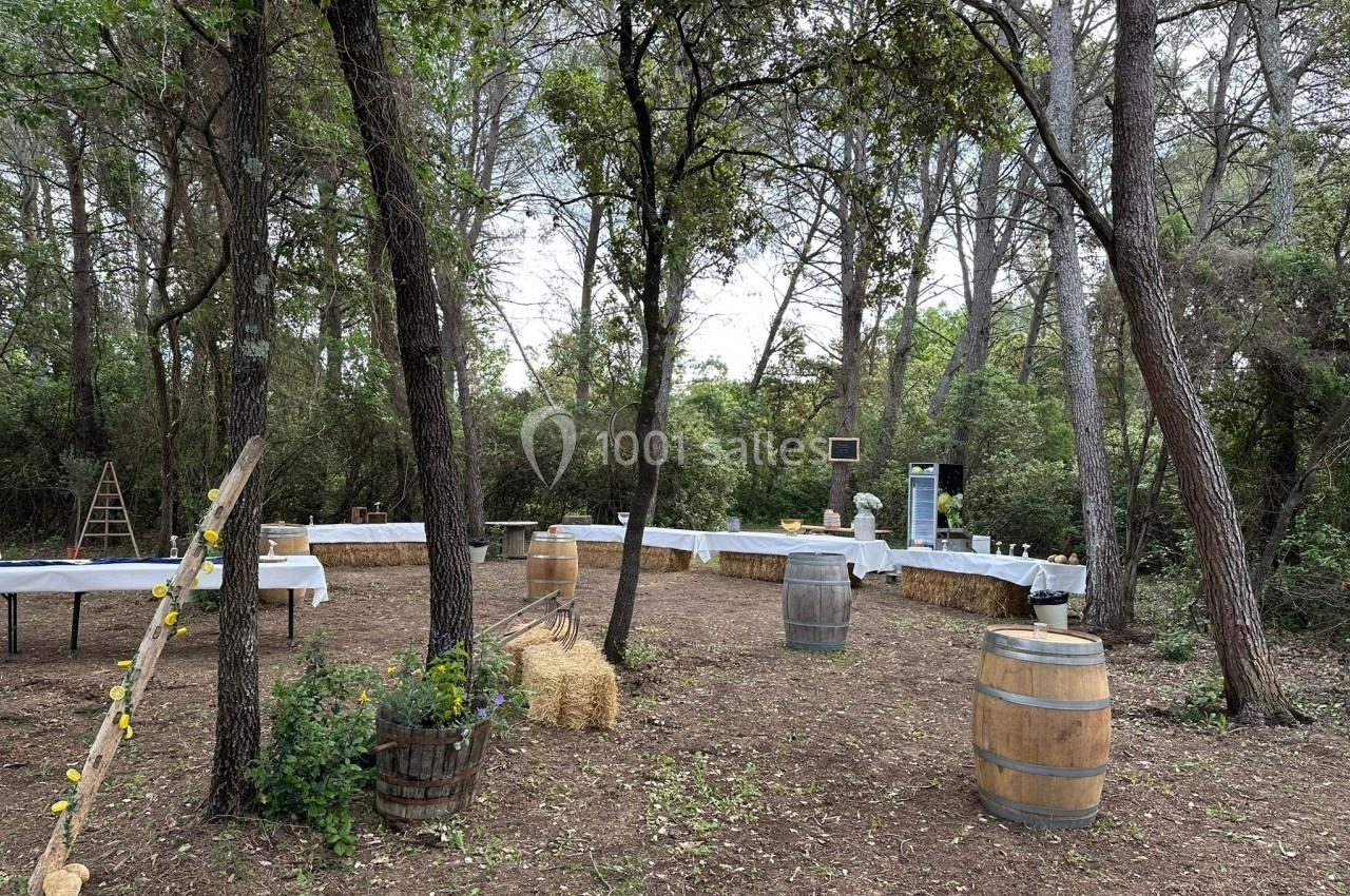 Espace extérieur aménagé avec tables, bottes de paille et tonneaux, entouré d'arbres dans une ambiance champêtre.