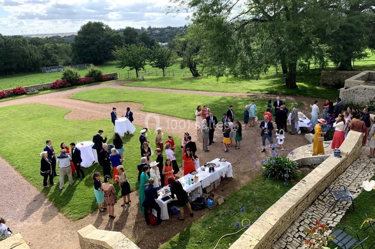 Groupe de personnes rassemblées dans un jardin pour un événement en plein air, entouré de verdure et de murs en pierre.