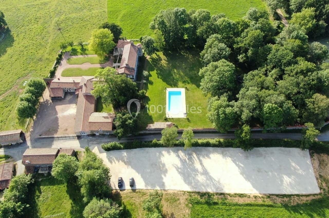 Vue aérienne d'une propriété rurale avec bâtiments, piscine, pelouse, arbres et chemin bordé de verdure.