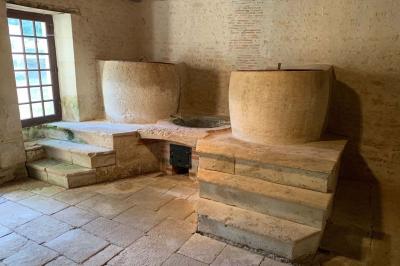 Vue sur un jardin avec pelouse, allées en gravier, parterre de fleurs rouges et bâtiments en pierre sous un ciel dégagé.