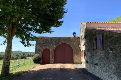 Vue sur un jardin avec pelouse, allées en gravier, parterre de fleurs rouges et bâtiments en pierre sous un ciel dégagé.