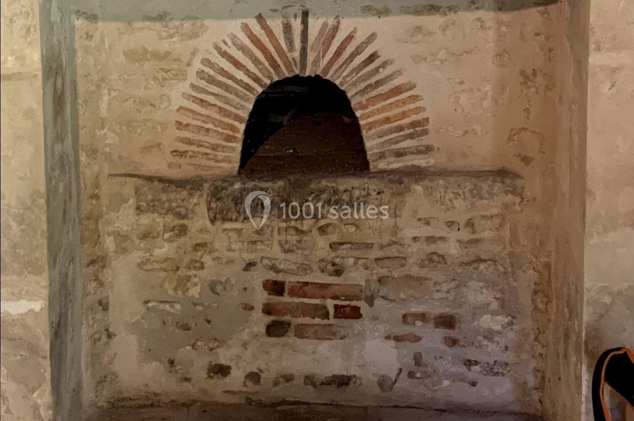 Ouverture voûtée en briques rouges dans un mur en pierre, évoquant un ancien four ou une cheminée.
