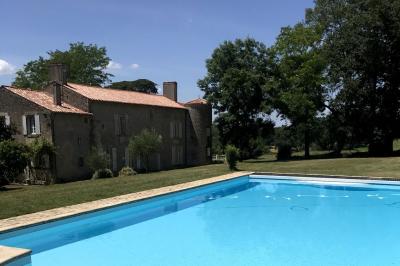 Vue sur un jardin avec pelouse, allées en gravier, parterre de fleurs rouges et bâtiments en pierre sous un ciel dégagé.