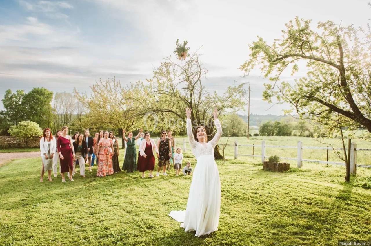 Une mariée lance son bouquet dans un jardin verdoyant, entourée d'invités prêts à l'attraper.
