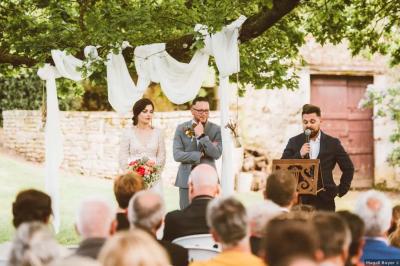 Vue sur un jardin avec pelouse, allées en gravier, parterre de fleurs rouges et bâtiments en pierre sous un ciel dégagé.