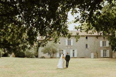 Vue sur un jardin avec pelouse, allées en gravier, parterre de fleurs rouges et bâtiments en pierre sous un ciel dégagé.