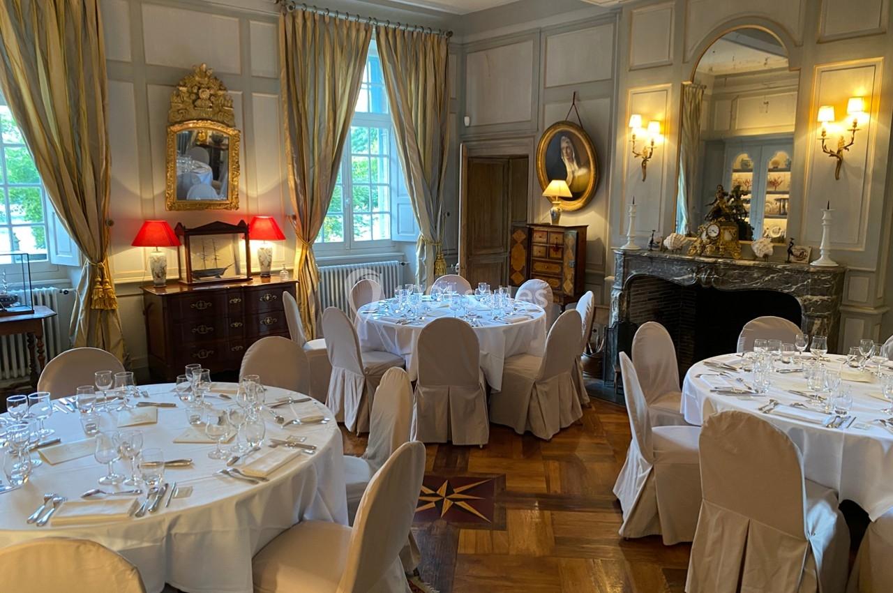 Salle élégante avec tables rondes dressées pour un repas, décorée de rideaux dorés, miroirs et mobilier classique.