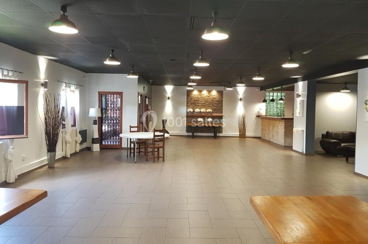 Salle spacieuse avec sol en carrelage, tables en bois, éclairage suspendu et décoration sobre.