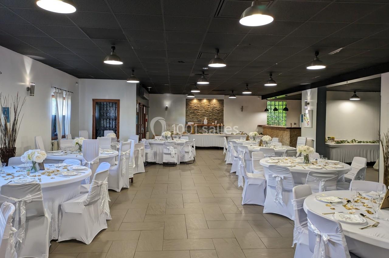 Salle de réception décorée avec des tables rondes, nappes blanches et chaises couvertes, prête pour un événement.