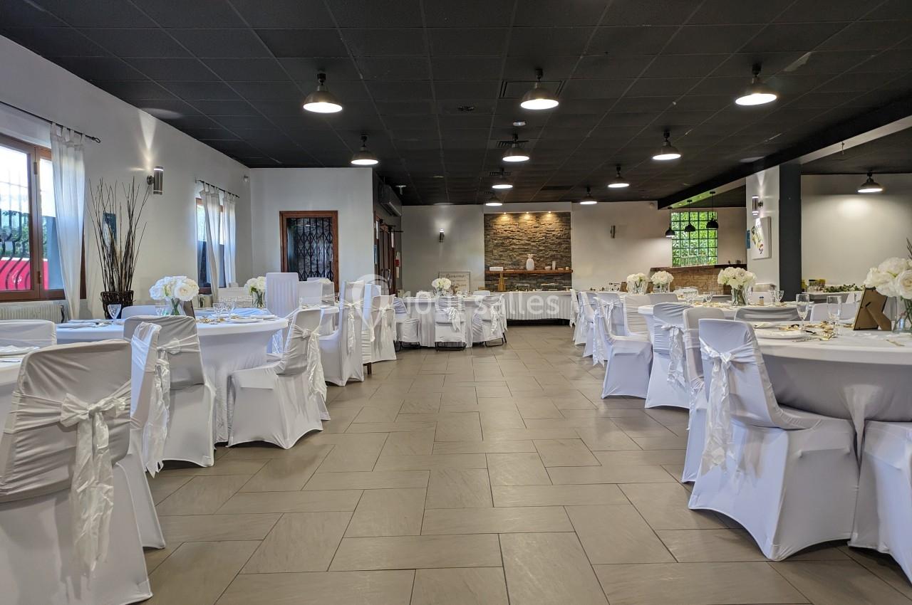 Salle de réception décorée avec des tables rondes, nappes blanches et chaises couvertes de housses blanches.