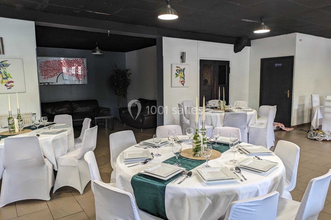 Salle de réception avec tables rondes dressées, nappes blanches, décorations vertes et chaises recouvertes.