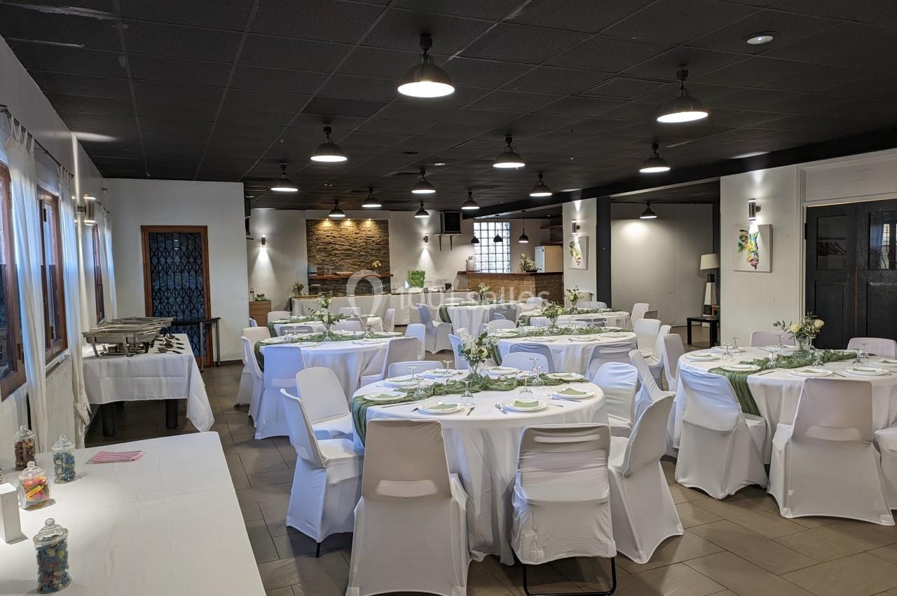 Salle de réception décorée avec des tables rondes dressées, nappes blanches et éclairage suspendu.