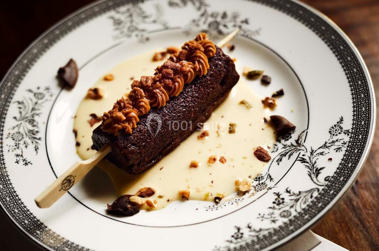 Dessert sur bâtonnet avec ganache au chocolat, noix concassées et sauce vanille, présenté sur une assiette décorée.