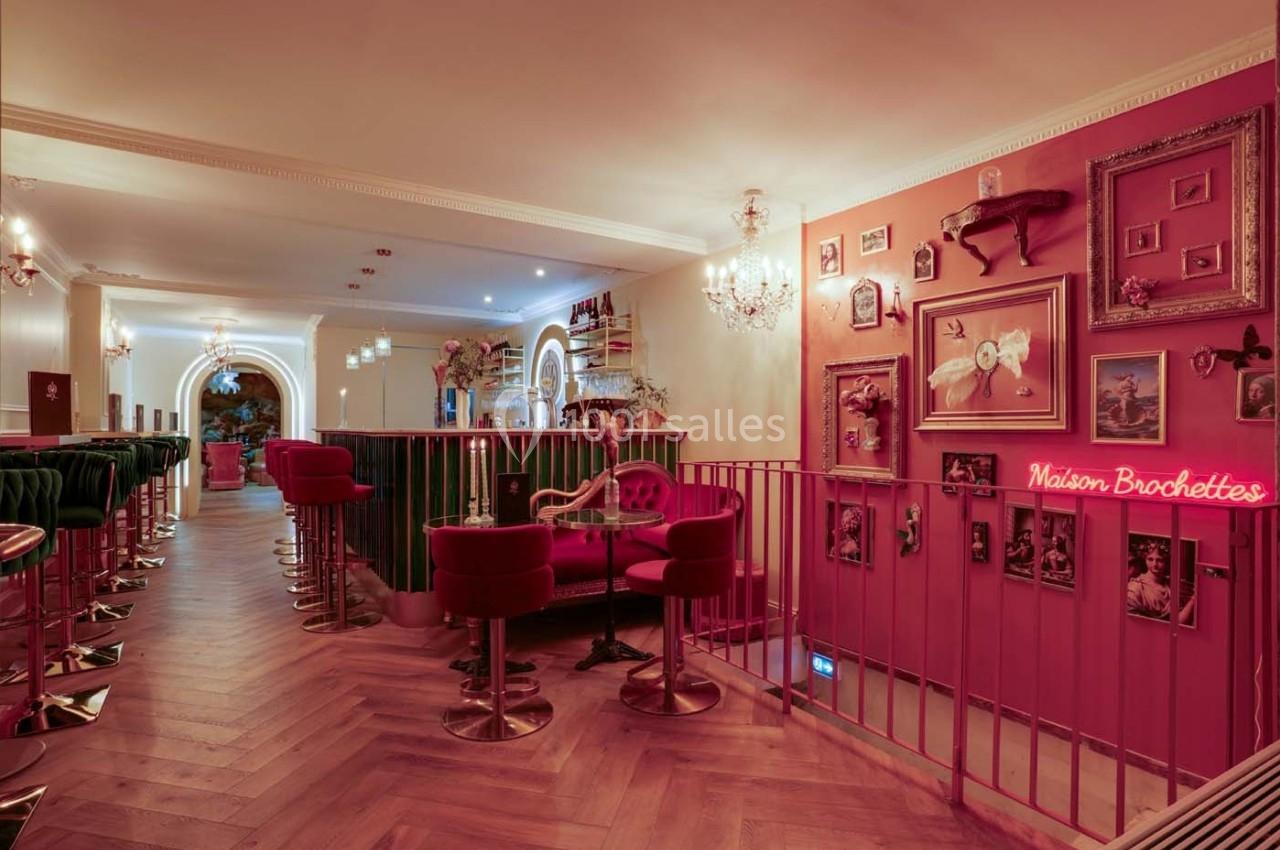 Intérieur d'un restaurant avec des fauteuils rouges, un bar, des décorations murales et une enseigne lumineuse rose.