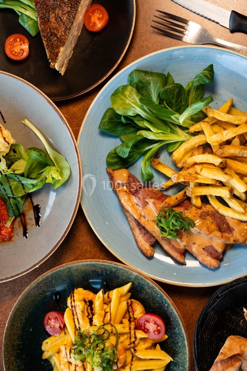 Assortiment de plats comprenant viande, frites, salade et garnitures variées, présenté sur une table en bois.